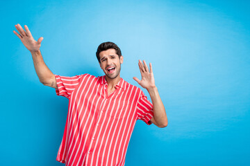 Poster - Photo of good mood positive man with bristle dressed striped shirt raising palms up sing song dancing isolated on blue color background