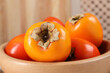 Delicious ripe persimmons in bowl on blurred background, closeup