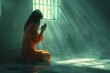 Female prisoner in an orange jumpsuit with dark long hair sits in meditation, in the rays of the sun penetrating through the prison bars.