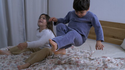 Joyful child bouncing in bed captured in mid-air in super slow motion at 1000 fps, speed-ramp of young boy jump and up and down next to sister