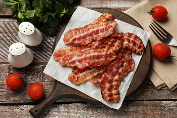 Fried bacon slices, tomatoes, parsley and spices on wooden rustic table, flat lay