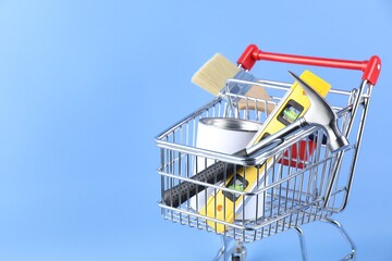 Canvas Print - Small shopping cart with paint and renovation equipment on light blue background. Space for text