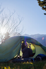 Sticker - child sits in a tent and drinks water from a bottle. boy in a sleeping bag. portrait of a child in a tent.  camping and trekking with children.