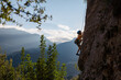 © zhukovvvlad - Children's rock climbing. A boy climbs a rock against the backdrop of mountains. Extreme hobby. Athletic child training to become strong.