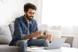 © Prostock-studio - Content indian man browsing smartphone and holding mug of coffee at home