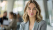 © MP Studio - A young professional woman with blonde hair, wearing a grey blazer, is smiling subtly at the camera in a well-lit office setting.