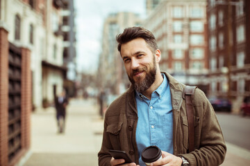 Man drinking coffee and using smartphone on city street