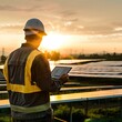 © Attila - a solar technician from behind, looking over a field of solar panels while holding a tablet