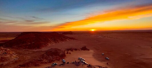 panoramic view from the top of the hill over the red sand desert and canyons, crossed by off-road cars at sunset. Timimoun, Algeria