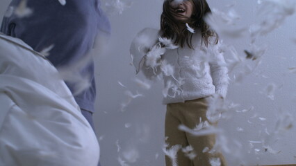 Siblings having pillow fight while bouncing in bed captured in super slow motion at 1000 fps with feathers flying mid-air everywhere, happy carefree childhood emotion