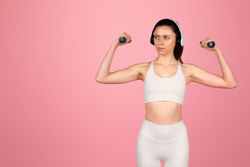 Wall Mural - Focused young woman in white athletic wear flexing muscles with dumbbells