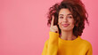 With playful charm, a woman in a yellow sweater points upwards, her curly hair and bright expression against a pink background illustrating a lighthearted and creative mood.
