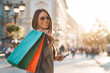 Attractive female holding colorful shopping bags on her shoulder while walking down the street on sunny afternoon and looking at camera with a smile.