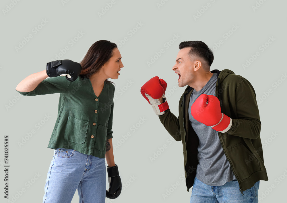 Young couple in boxing gloves quarreling on light background