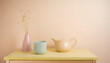 Stilleben, neutraler Hintergrund, gelbe Oberfläche eines Buffets mit einer Vase, einer Tasse und einer Teekanne, zarte Pastellfarben, minimalistisch mit viel Freifläche