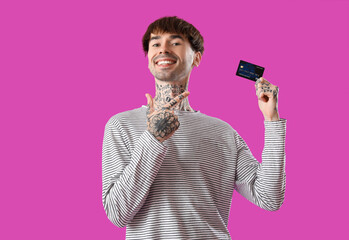 Sticker - Tattooed young man pointing at credit card on purple background