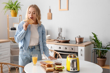 Wall Mural - Young beautiful woman eating tasty toast with peanut butter in kitchen