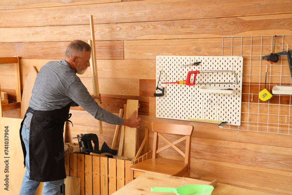 Mature carpenter with wooden planks in workshop