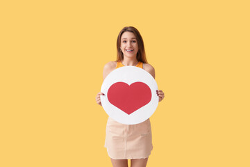 Pretty young woman holding heart like icon on orange background