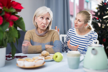 Wall Mural - Adult daughter explains something to a mature dissatisfied mother, sitting at the table