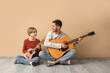 © Pixel-Shot - Private music teacher and little boy with guitars sitting on beige background