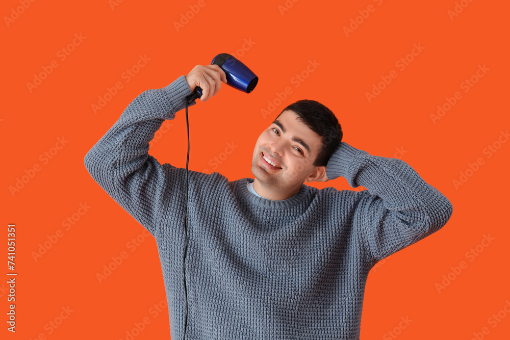 Handsome young man with hair dryer on orange background