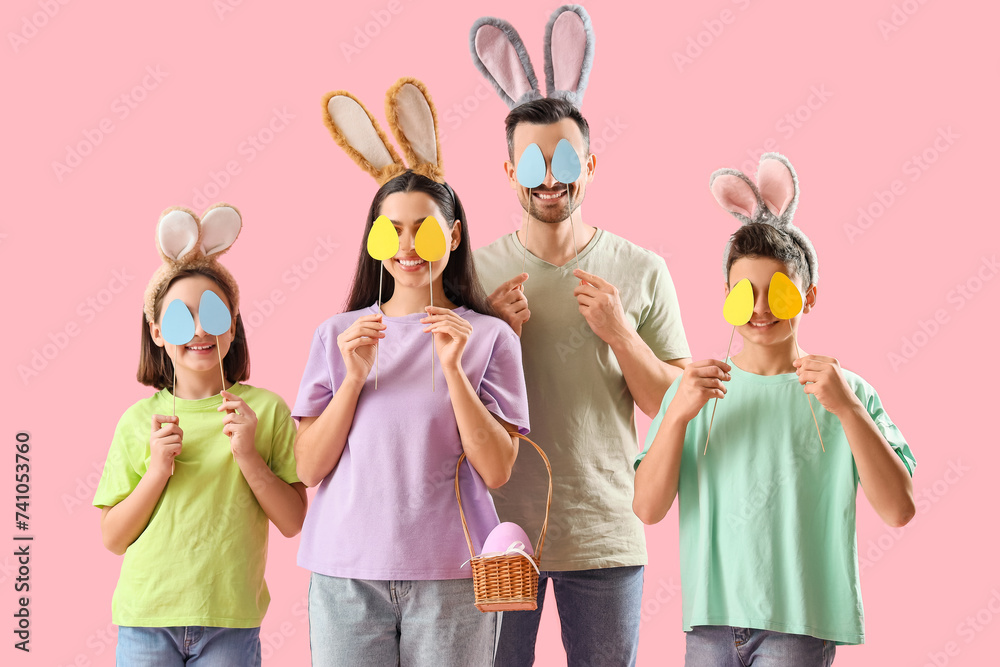 Happy family in bunny ears with paper Easter eggs on pink background