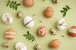 Decorated Easter eggs, chamomiles and leaves on green background