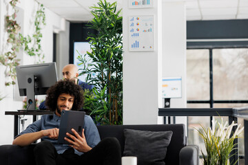 Poster - Company project manager scrolling social media on digital tablet while relaxing in business office. Arab smiling financial analyst browsing internet and messaging online at workplace