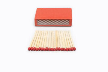 Matches in front of a red matchbox isolated on a white background. Close-up of red matches with space for text. Red matches are laid out in an even row on a white background