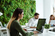 © Наталья Лазарева - young woman is working at laptop in modern office with a living green vertical wall of moss,concept of sustainable development, caring for planet, climate change, increasing oxygen levels, air quality