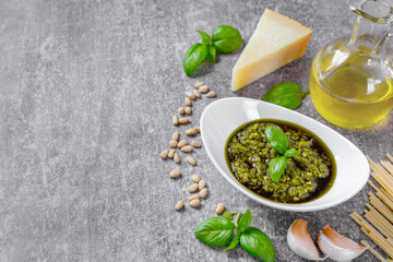 Wall Mural - Homemade pesto sauce in small white round jar and ingredients for pasta on gray stone concrete with copy space. Traditional Italian cuisine, recipe, restaurant menu