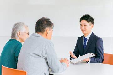 Canvas Print - 高齢者夫婦に申請書類の説明をするスーツ姿の男性（ソーシャルワーカー・介護・ケアマネジメント）
