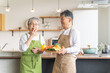 家のキッチンの前で笑顔で話すアジア人高齢者夫婦（料理教室）

