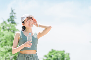 Wall Mural - 公園で水・ミネラルウォーターを飲む女性（水分補給・運動・ワークアウト・ランニング・ウォーキング）
