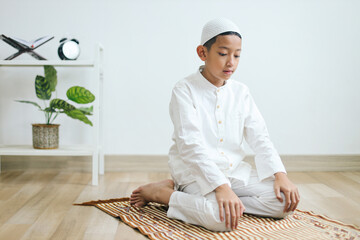 Wall Mural - Young muslim boy praying on prayer mat and doing one of movement gesture in salat procedure. 