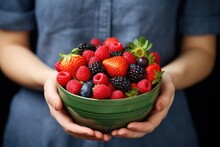 Girl is holding a bowl with various ripe healthy berries