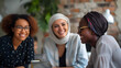 © Kanlayarawit - Women empower each other in a workplace on a blurred colorful background. Diversity of nationality, Arab and black women. Three businesswomen are sitting in a meeting room with a tablet.