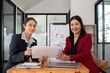 © chartchai - Two businesswomen discussing project strategy in office conference room Businesswoman discusses project planning with colleagues in modern workplace, gives advice on financial data report