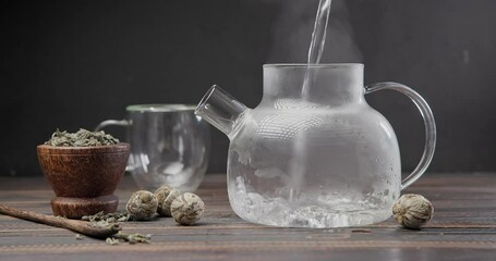 Wall Mural - Hot boiling water pours into glass teapot with blooming flower tea on wooden background