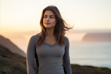 Sticker - Portrait of a beautiful young woman with long brown hair, wearing a gray T-shirt, standing in front of the sea and looking into the camera.