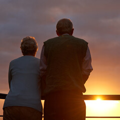 Wall Mural - Senior couple, sunset and together on balcony in outdoors, bonding and love on vacation or holiday. Back, elderly people and dusk on terrace and together in nature, security and travel for marriage