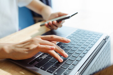 Woman using smartphone and hand typing on the computer keyboard in the office.