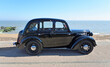 Classic  Black Austin 8 Saloon parked on seafront promenade beach and sea in background.