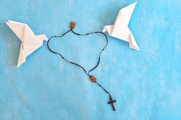 Wall Mural - White dove origami carrying rosary or scapular in sky blue background.