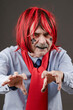 An ugly old man with terrible makeup in a red wig stretches his dirty scary hands forward.