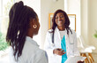 Friendly dark-skinned female doctor therapist giving medical advice during meeting in her office. Woman in white coat holding clipboard and talking to female patient. Medical healthcare concept.