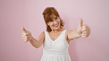 Canvas Print - Joyous middle-aged woman gesturing thumbs up, celebrating triumphant success with a merry smile, standing isolated over a pink background in her trusty dress.