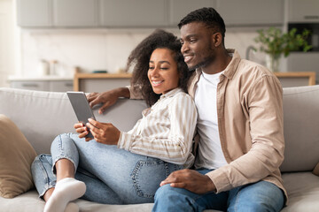 Wall Mural - Happy black couple browsing online together on digital tablet indoor