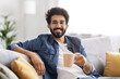 © Prostock-studio - Cheerful young indian man wearing glasses and shirt, enjoying cup of coffee